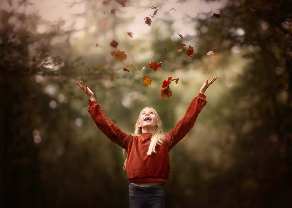 herfst portret van een blond meisje dat blaadje in de lucht gooit in het bos door natuurlijk licht fotograaf willie kers uit Apeldoorn