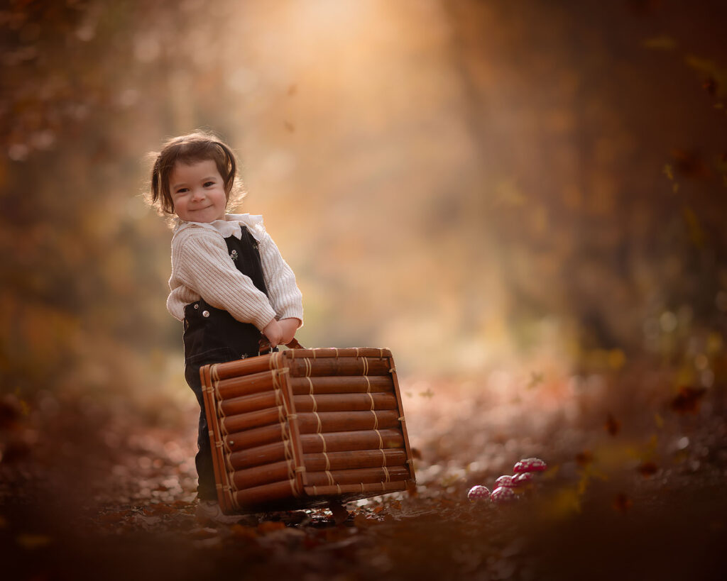 herfstportret van een peuter met een koffer bij paddestoelen in het bos door natuurlijk licht fotograaf willie kers uit apeldoorn