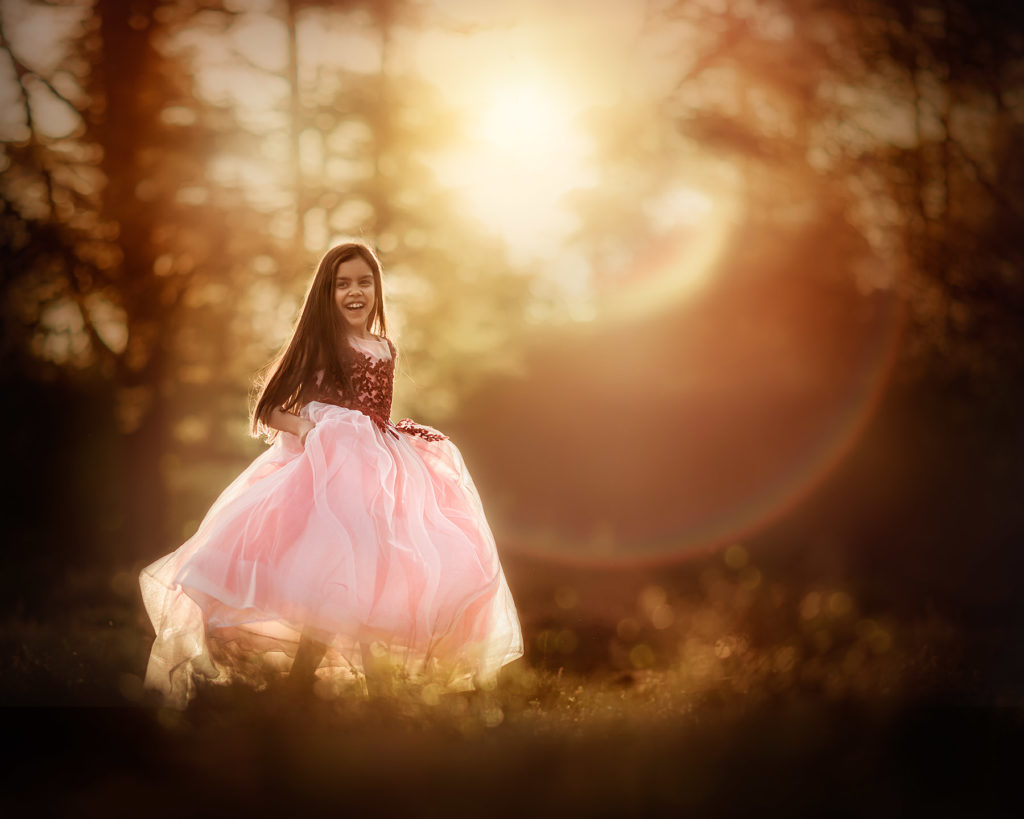 portret van een heel blij meisje in een rose prinsessenjurk die danst in het bos tijdens zonsondergang door natuurlijk licht fotograaf en workshops Willie Kers uit Apeldoorn