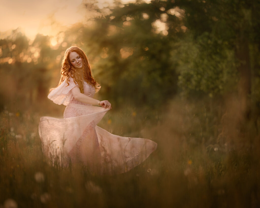 Canon-fine-art-portret-van-een-roodharige-vrouw-dansend-in-het-gras-in-een-roze-trouwjurk-tijdens-zonsondergang-door-natuurlijk-licht-fotograaf-Willie-Kers-uit-Apeldoorn