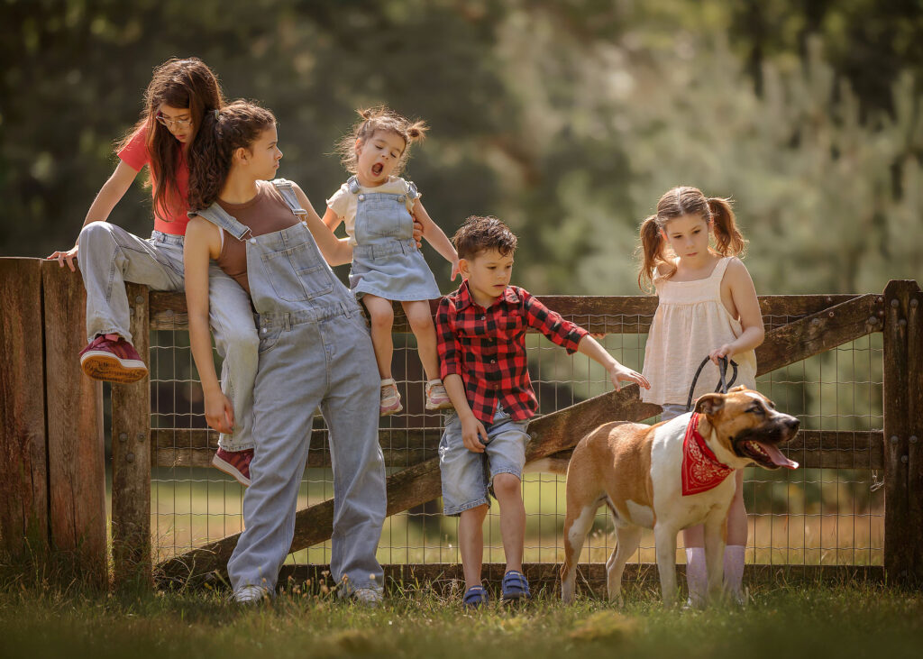 fine art portret van 5 kinderen in jeans zittend op een hek met hun hond die een boerenzakdoek omheeft terwijl ze spelen door fotograaf willie kers uit apeldoorn copy